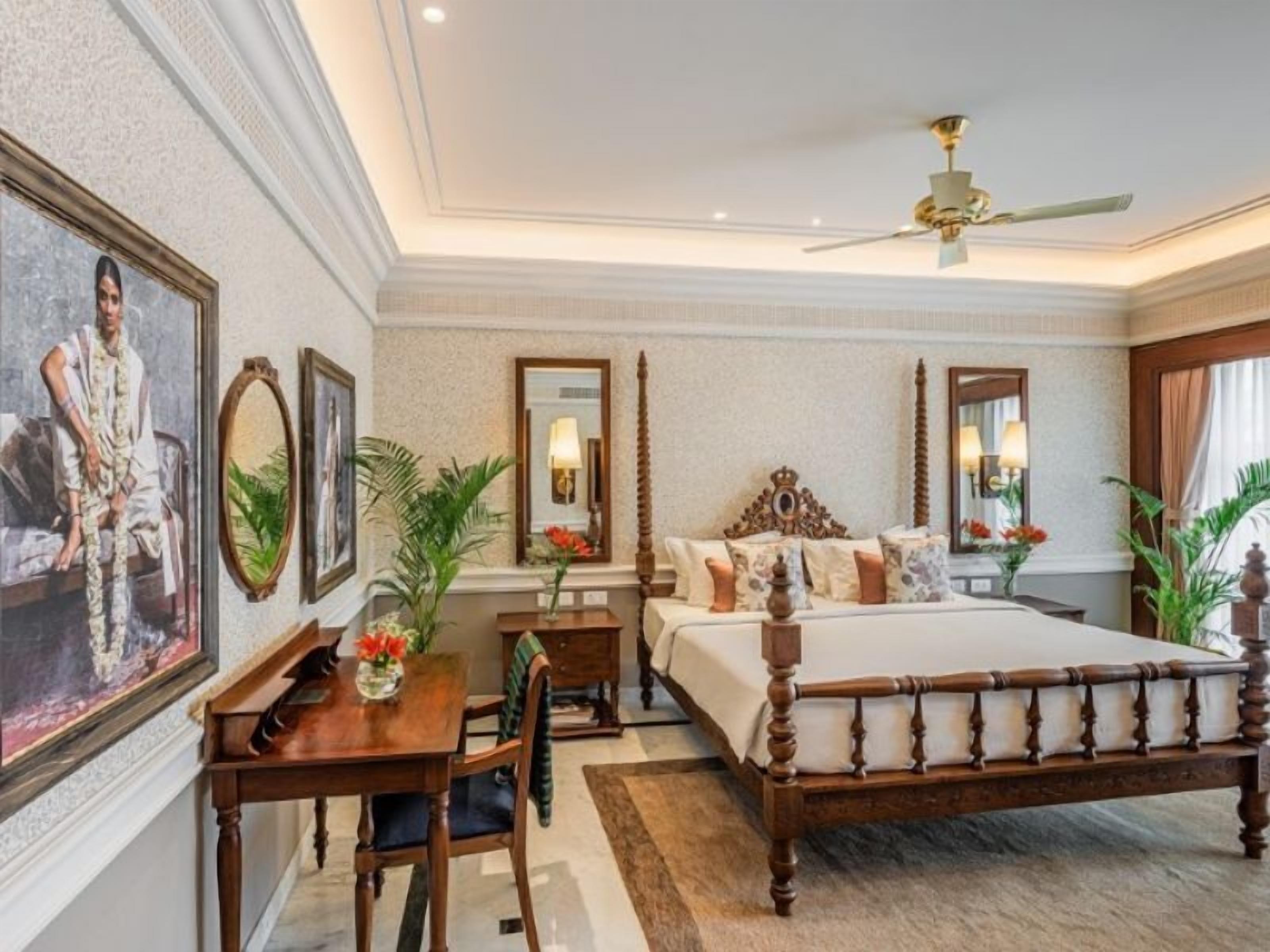 A spacious bedroom with a large bed, a desk, and a chair. There are multiple mirrors and a ceiling fan.