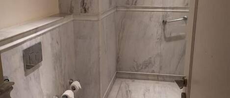 A bathroom with a toilet, a shower, and marble walls.