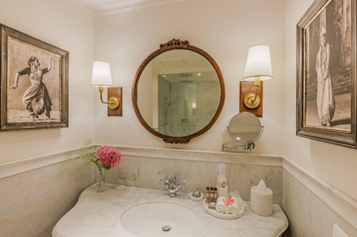 A bathroom with a marble sink, two wall-mounted mirrors, and framed pictures on the walls.