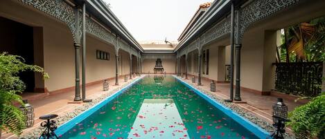 A pool with a central walkway, surrounded by ornate columns and a tiled floor.