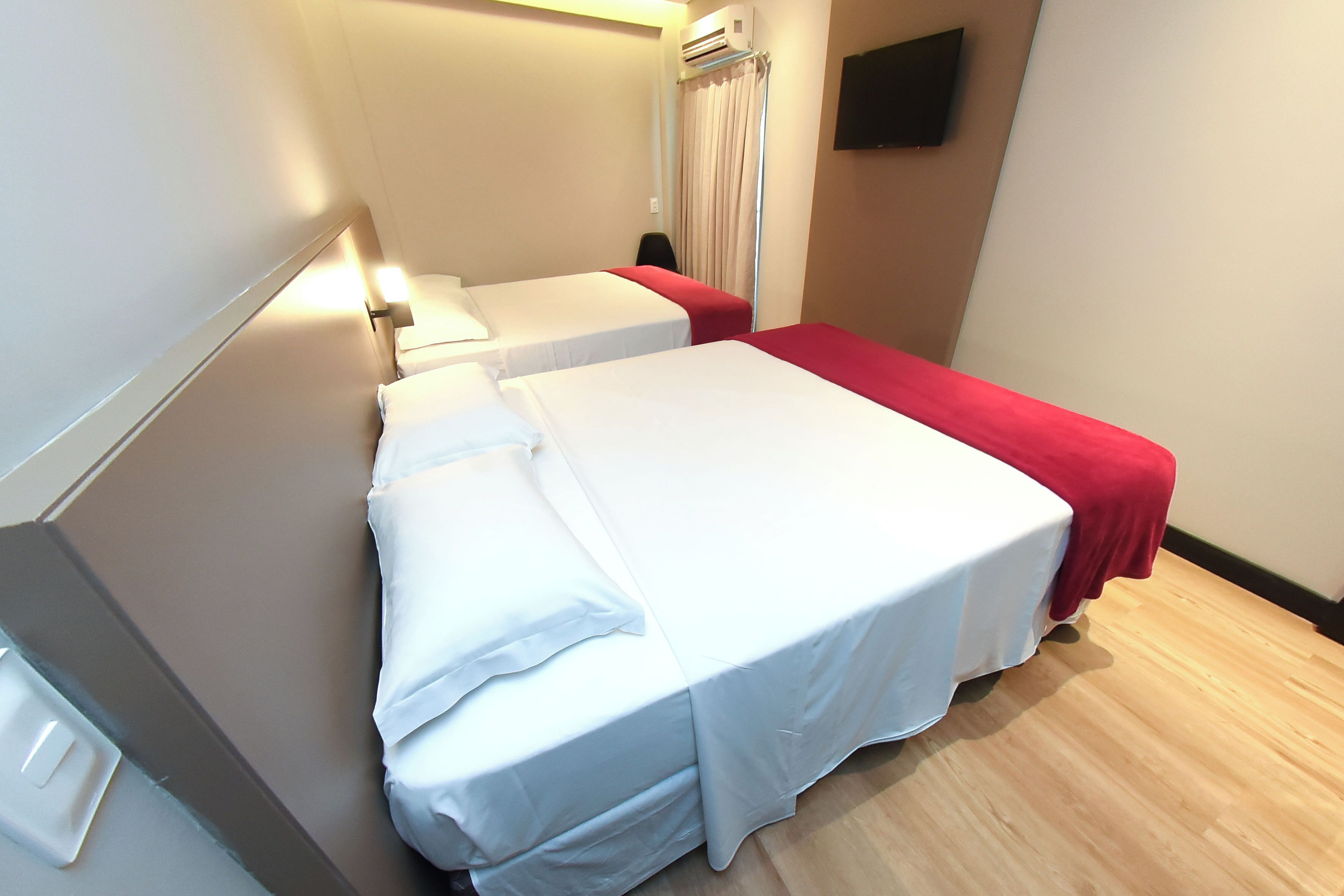 A hotel room with two beds, a flat-screen TV mounted on the wall, and a window with curtains.