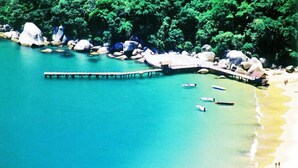 A coastal area with a pier extending into turquoise water, surrounded by large rocks and dense greenery. - Arco do Sol Parque Hotel (Camboriú)