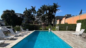 A rectangular swimming pool with tiled edges, surrounded by lounge chairs and a paved deck. - Arco do Sol Parque Hotel (Camboriú)