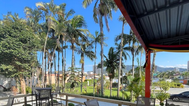 A wooden deck with outdoor furniture, palm trees, and a view of buildings and mountains in the background. - Arco do Sol Parque Hotel (Camboriú)