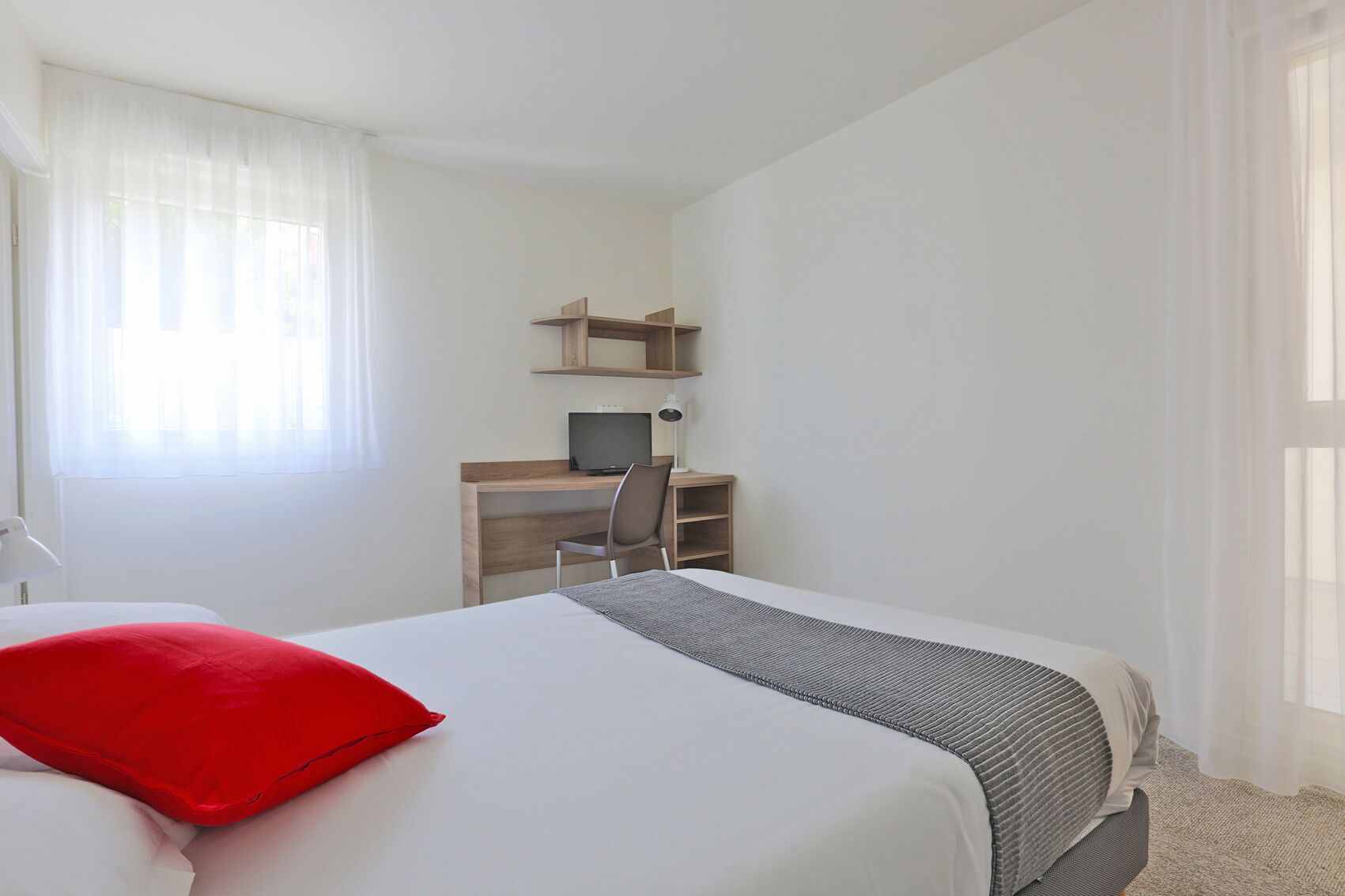 A hotel room with a bed, a desk with a computer, and a chair.