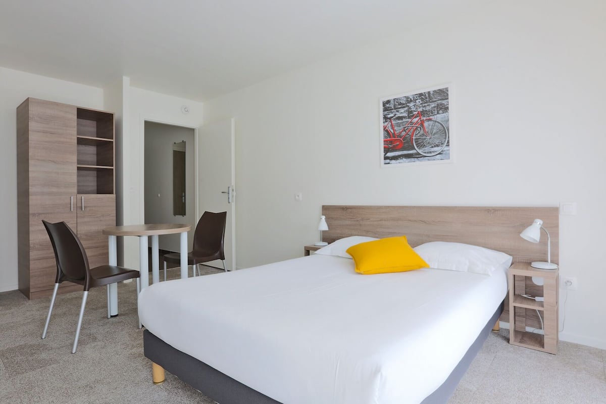 A hotel room with a bed, a desk, a chair, a wardrobe, and a wall-mounted picture.