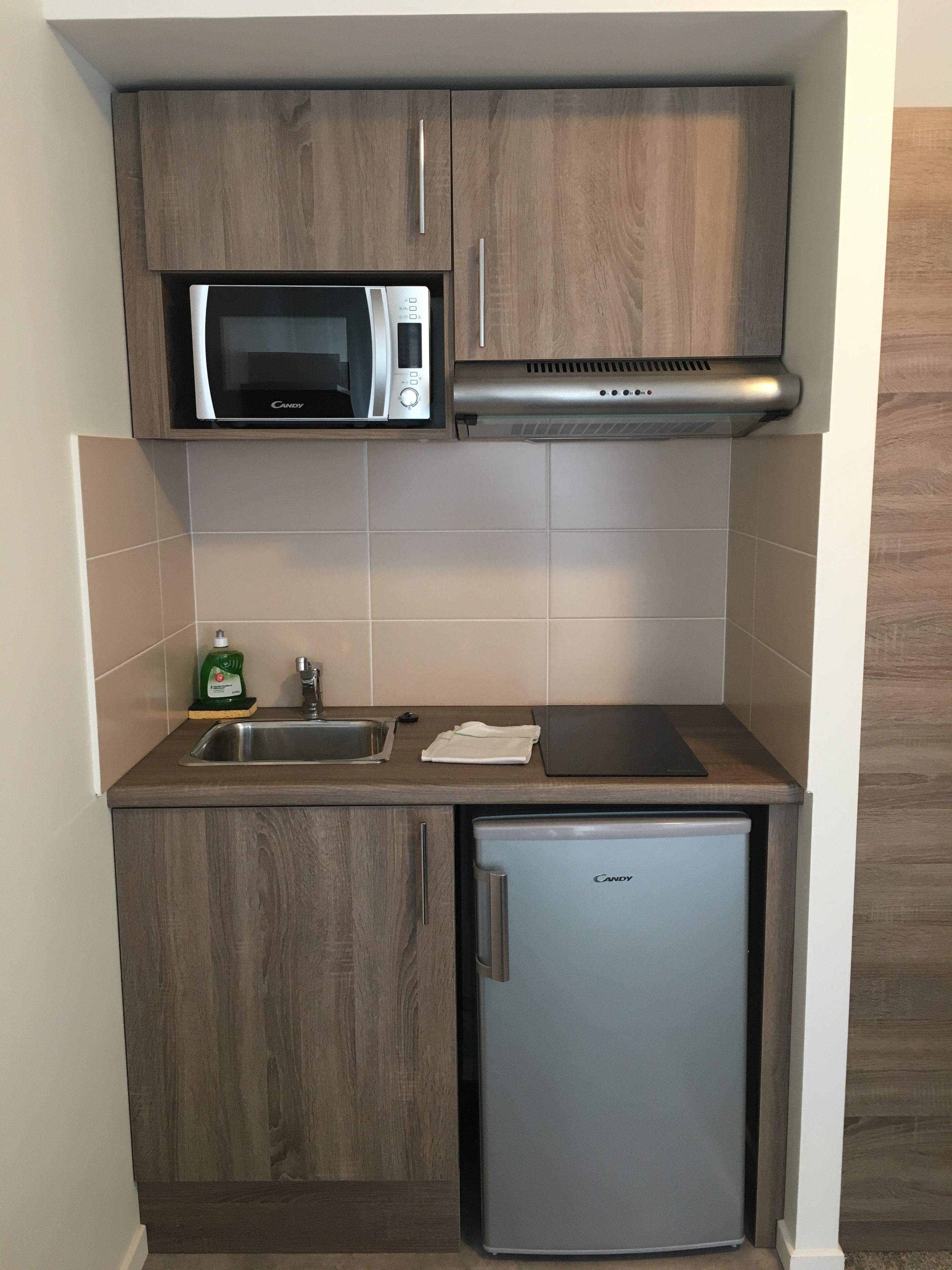 Cocina compacta con microondas, horno integrado, fregadero y refrigerador.