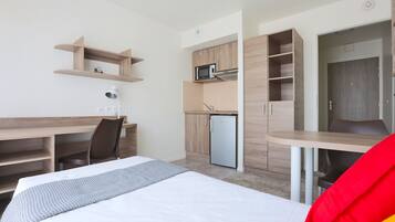 Hotellihuone, jossa on sänky, työpöytä, tuoli, pieni keittiö ja vaatekaappi.