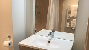 A modern bathroom with a white sink, a mirror, a shower, and a towel rack. - KOSY Appart’Hôtels – Art’ & Facts (Nancy)