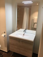 Uma casa de banho moderna com uma pia branca, um espelho, um chuveiro e um porta-toalhas.
