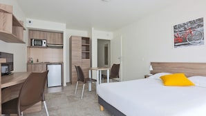 A hotel room with a bed, a desk, a chair, a microwave, and a small kitchenette. - KOSY Appart’Hôtels – Art’ & Facts (Nancy)