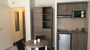 A compact kitchen with a microwave, sink, and a small refrigerator. There is a dining table with chairs and a magazine on it. - KOSY Appart’Hôtels – Art’ & Facts (Nancy)