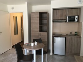 Cocina compacta con microondas, lavamanos y refrigerador pequeño. Hay una mesa de comedor con sillas y una revista encima.