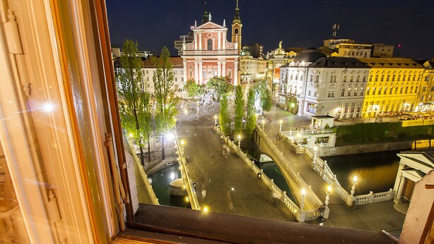 A view of a city square with a prominent church, a bridge, and surrounding buildings at night. - Filip Palace Luxurious Apartment (Ljubljana)