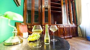 A room with a wooden cabinet, a table with a bottle of champagne, two wine glasses, a lamp, and a bowl of grapes. - Filip Palace Luxurious Apartment (Ljubljana)