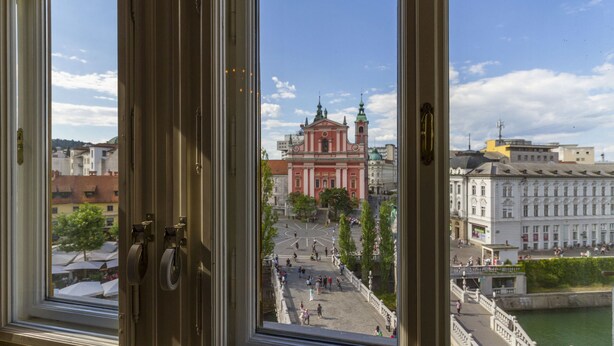 Une vue depuis une fenêtre donnant sur une place de la ville, avec un imposant bâtiment rouge et une rivière.