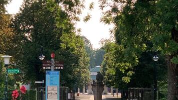 Ein Weg führt zu einem verschlossenen Eingang mit einer Statue in der Mitte, umgeben von üppiger Vegetation und einem Hinweisschild mit Informationen.