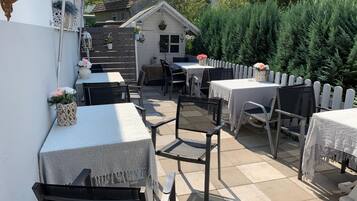 An outdoor patio with tables and chairs, a white picket fence, and a small building with a sloped roof.