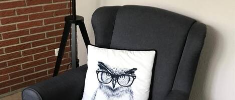 A black armchair with a white pillow featuring an owl illustration.