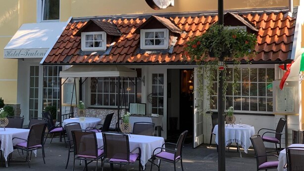 Restaurante com mesas ao ar livre, placa com 'Da Silvio' e um edifício do 'Hotel-Teutoni' ao fundo.