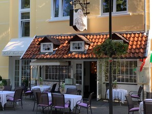 Un restaurant avec une terrasse, une enseigne indiquant « Da Silvio » et, au fond, le bâtiment de l’« Hôtel Teutoni ».