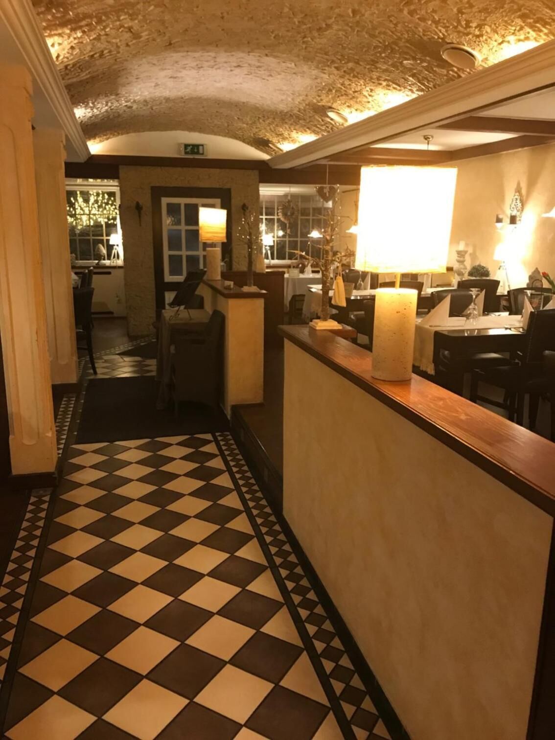A hotel lobby with a checkered floor, a reception desk, and a staircase leading to the upper floor.