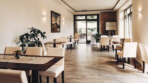 A spacious dining area with multiple tables and chairs, a large potted plant, and a view of the outdoors through large windows. - Gasthaus und Pension Alter Hafen (Zehdenick)