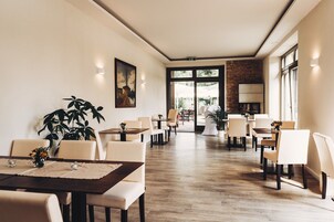 Un amplio comedor con varias mesas y sillas, una planta grande en maceta y vistas al exterior a través de ventanas grandes.