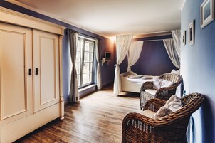 Una habitación con cama, sillas de mimbre, un armario y una ventana con cortinas.