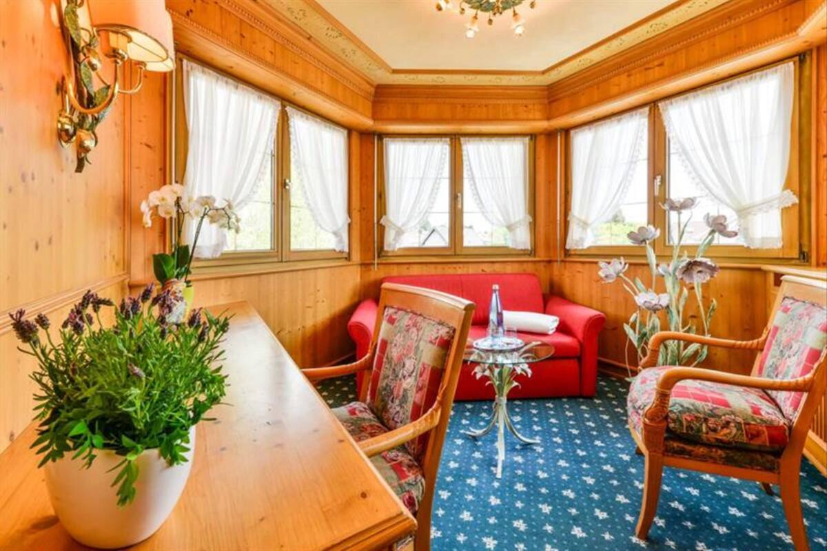A cozy room with wooden walls, a dining table, chairs, a red sofa, and large windows with curtains.