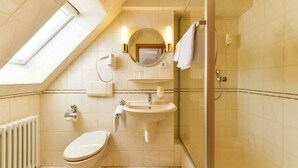 A compact bathroom with a skylight, a toilet, a sink, and a shower. - Hotel Jauch's Löwen (March)