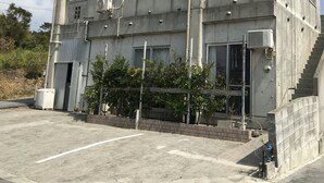 A concrete building with barred windows, air conditioning units, and a staircase leading to an upper level. - Biimata house (Nago)