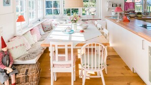 Una cocina luminosa con armarios blancos, una mesa de comedor de madera y un amplio ventanal que proporciona luz natural.