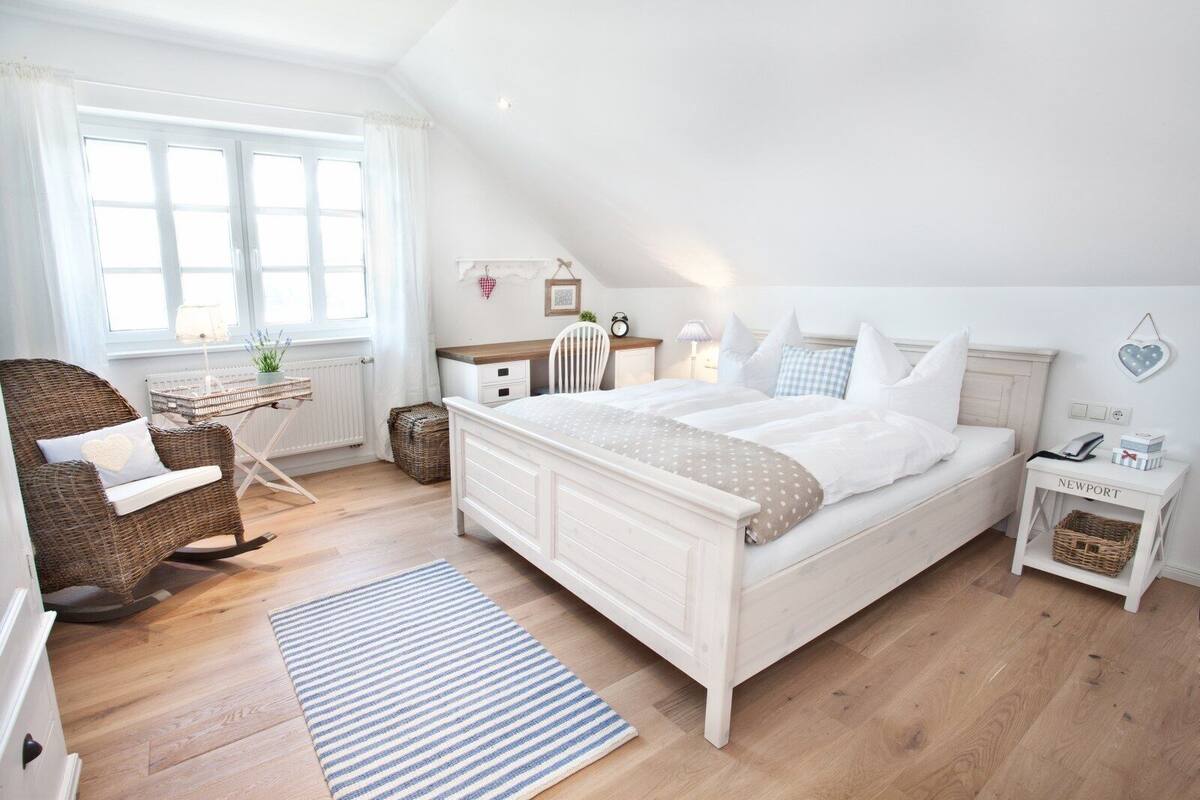 A bedroom with a large bed, a wicker chair, a desk, and a nightstand.