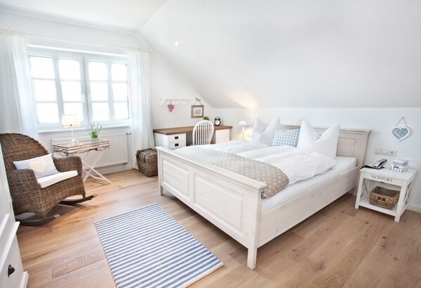 A bedroom with a large bed, a wicker chair, a desk, and a nightstand.