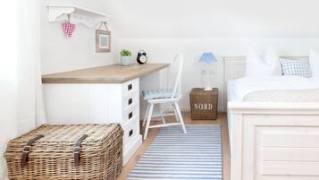 Ein Schlafzimmer mit einem Bett, einem Schreibtisch, einem Stuhl, einem Korbwäsche und einem blauen Teppich mit Streifen.