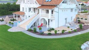 Una casa de dos plantas con techo de tejas rojas, un porche cubierto y un jardín ajardinado.