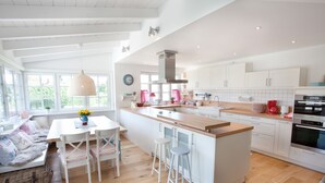 Una cocina luminosa con armarios blancos, una isla de madera y una zona de comedor con banco y sillas.