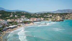 A coastal town with buildings along the beach, clear blue water, and mountains in the background. - Panorama Plus (Apokoronas)