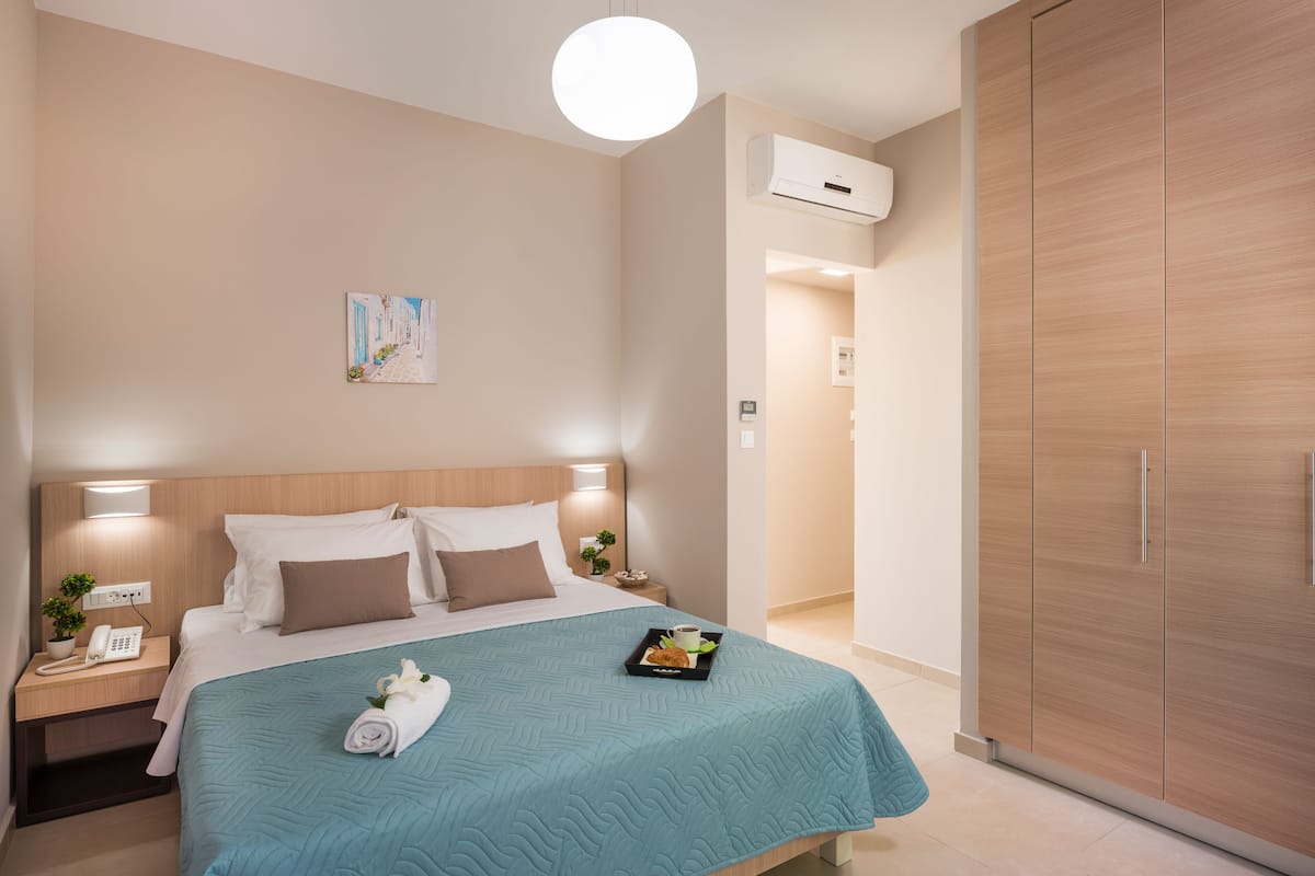 A neatly arranged hotel room with a bed, bedside tables, a wardrobe, and a wall-mounted air conditioner.