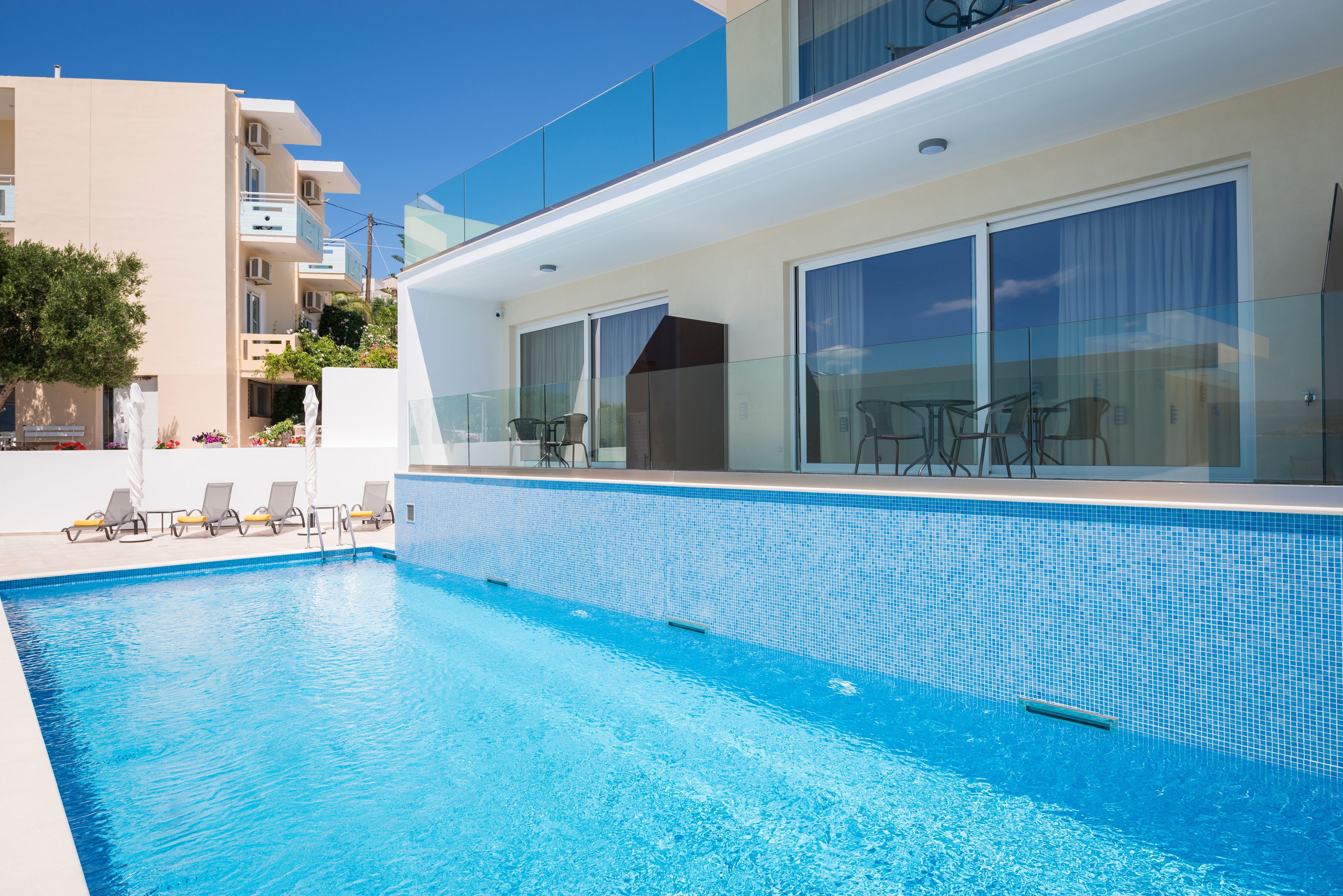 A modern hotel with a swimming pool, sun loungers, and a glass-enclosed balcony.