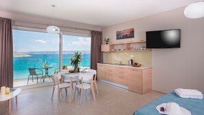 A modern hotel room with a balcony, a dining area, a kitchenette, and a bed with towels. - Panorama Plus (Apokoronas)