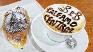 A croissant and a cup of coffee with latte art spelling "BER PALAEMO CENTRAL" on a white plate. - Palermo Central B&B (Palermo)