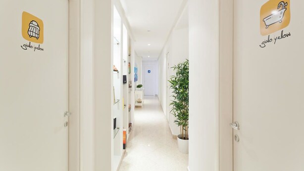 A hallway with white walls and doors, each marked with a logo and name. - Palermo Central B&B (Palermo)