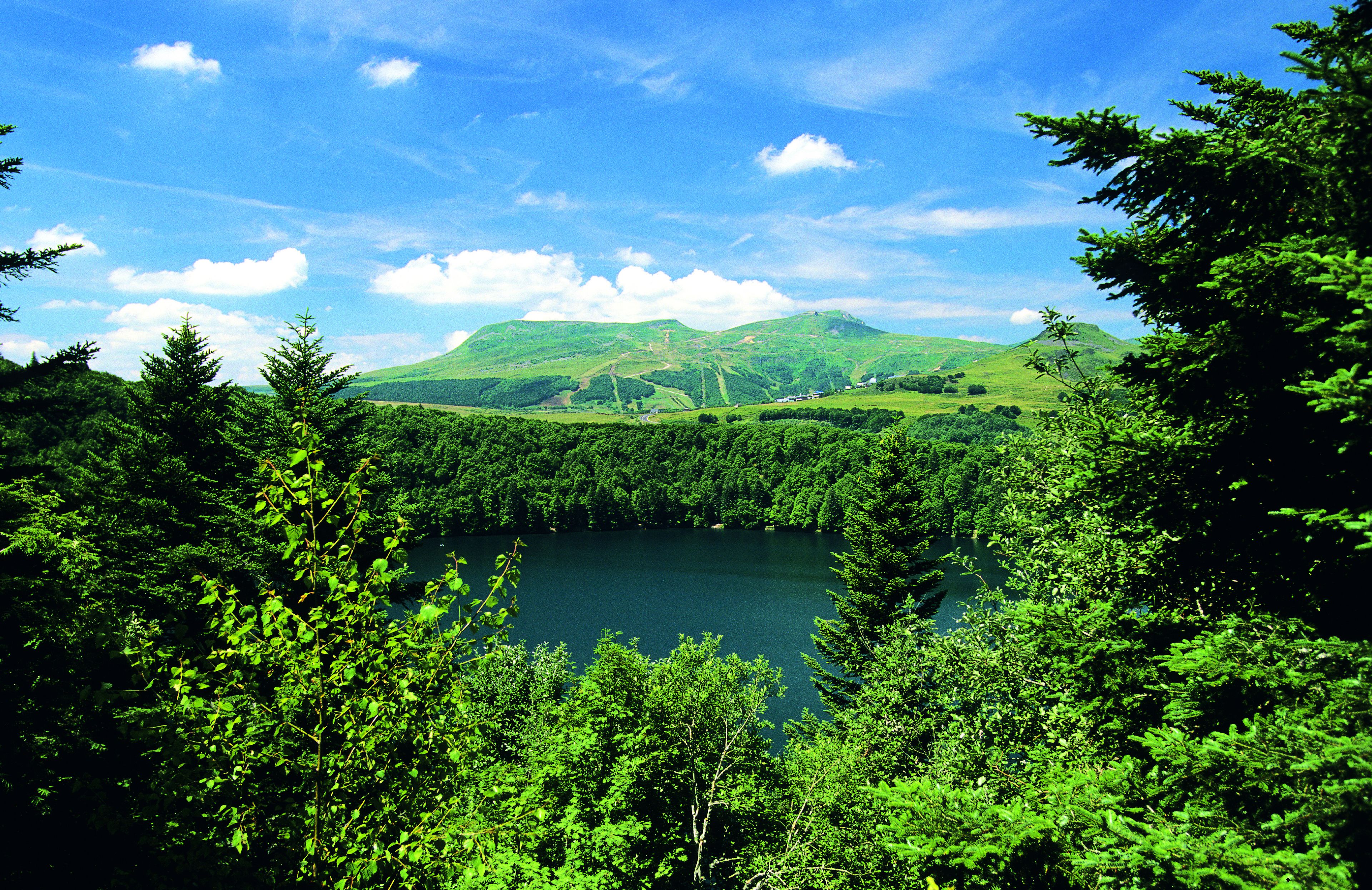 A lake surrounded by dense green forest and hills in the background.