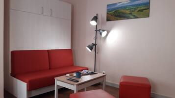 A modern living room with a red sofa, a small table, a floor lamp, and a painting on the wall.