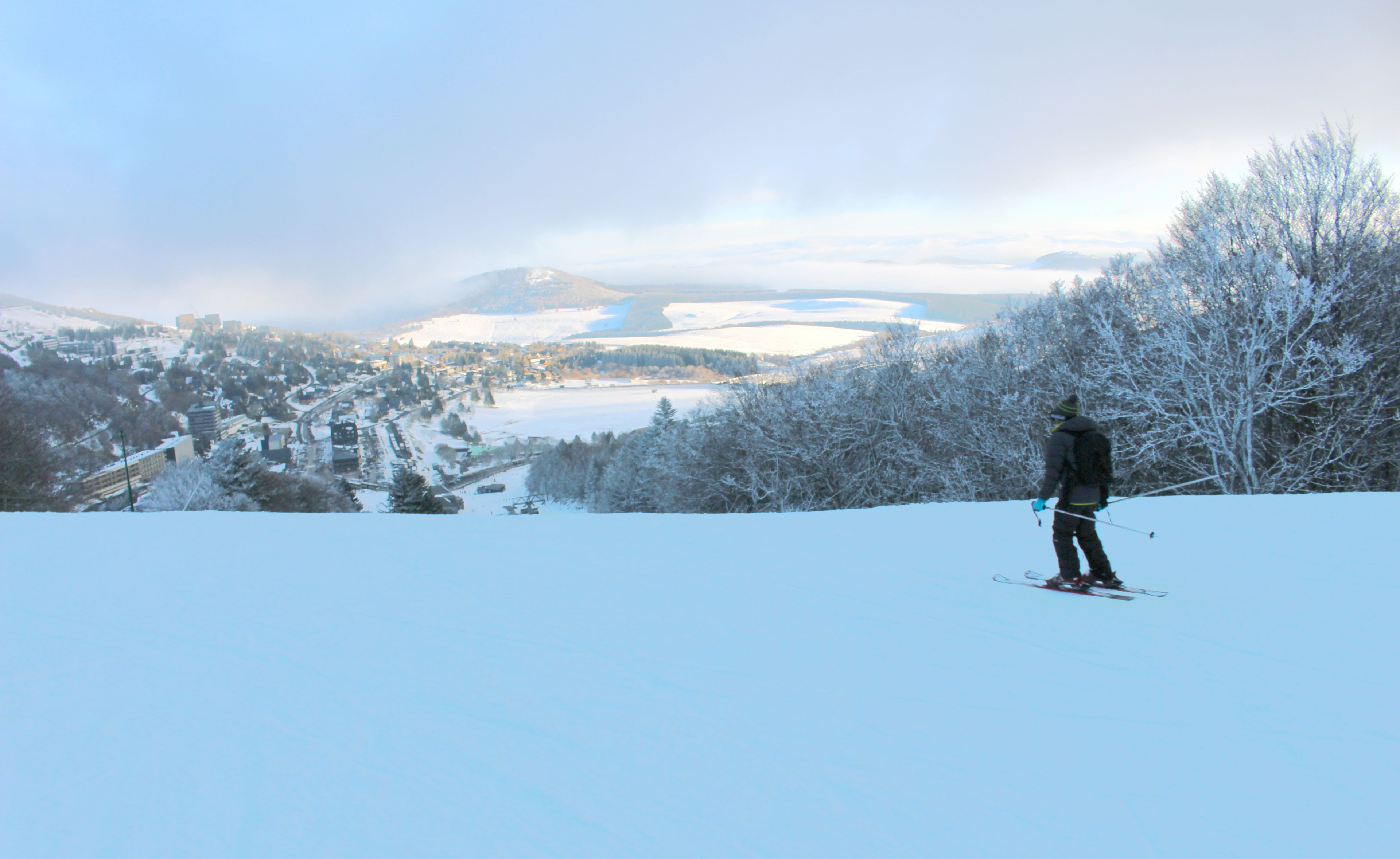 A person skiing on a snowy slope with a town and mountains in the background.