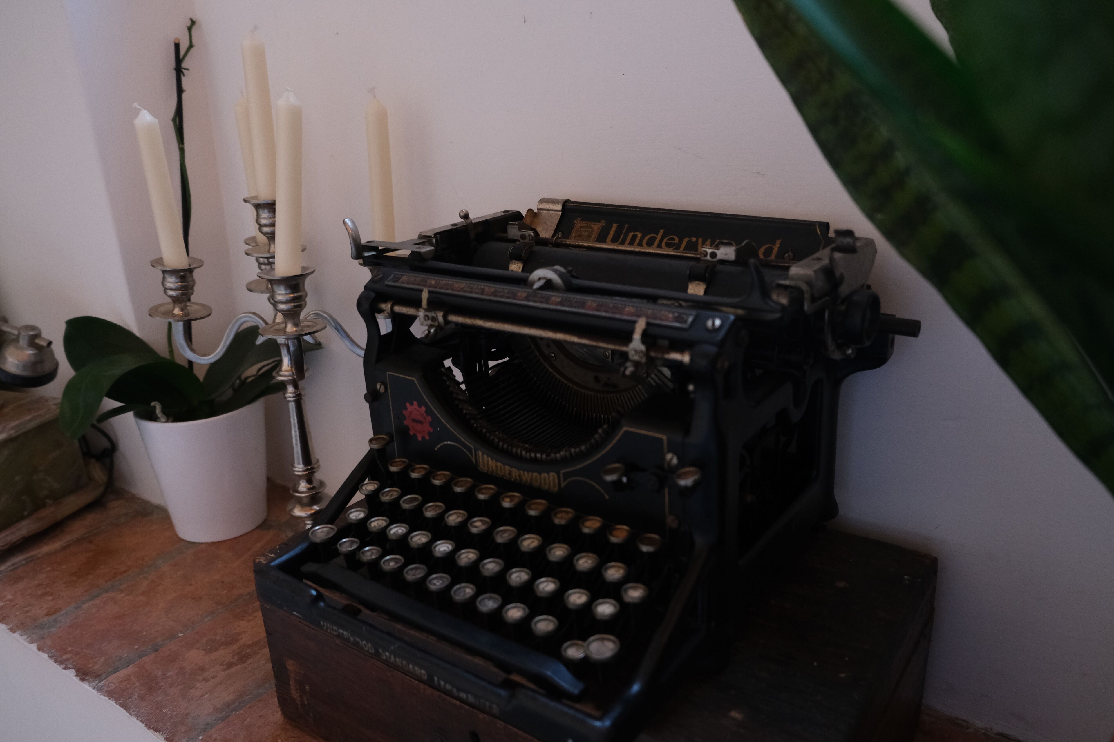 A vintage Underwood typewriter with four candles, a potted plant, and a small metal container on a wooden surface.
