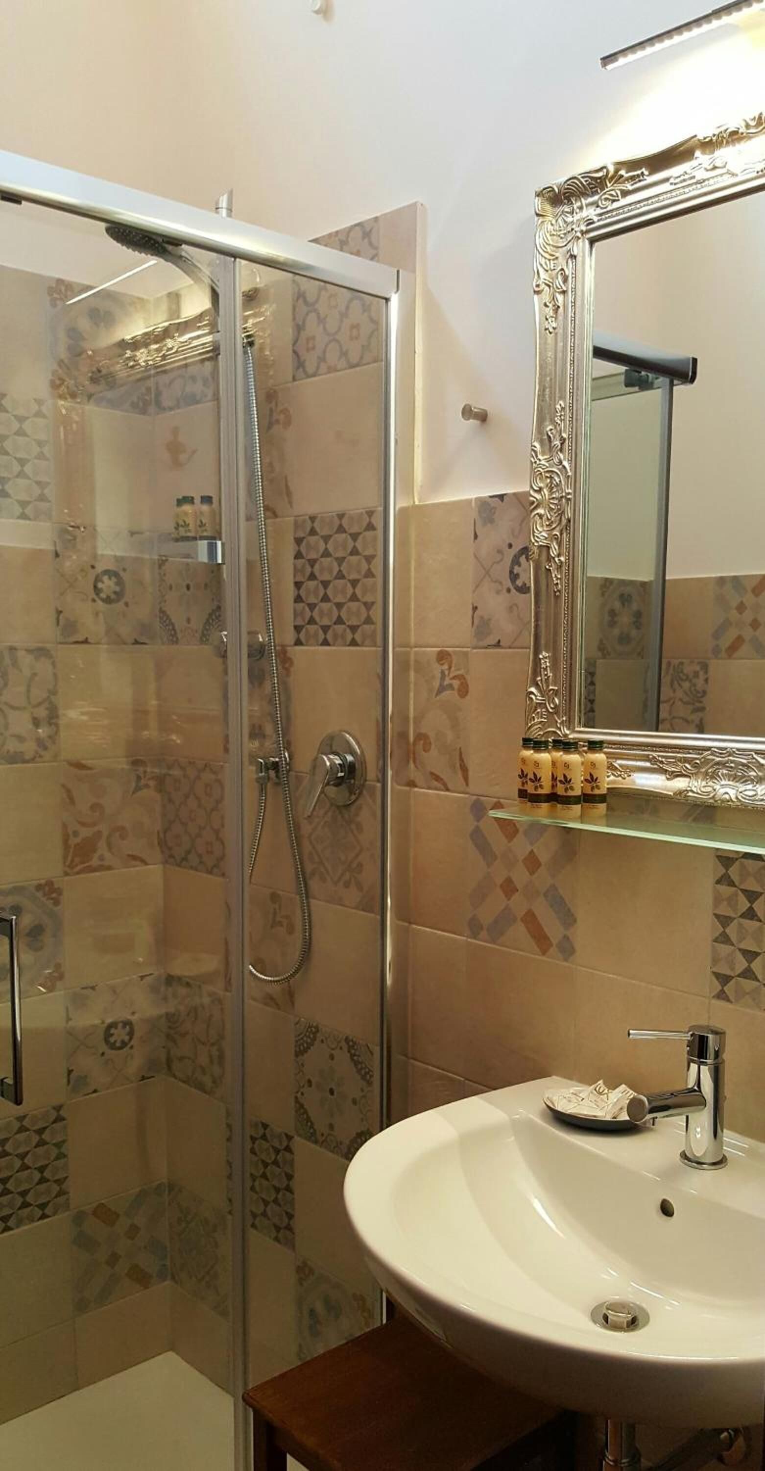 A bathroom with a glass-enclosed shower, a white sink, and a decorative mirror with an ornate frame.