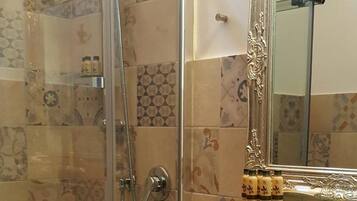 A bathroom with a glass-enclosed shower, a white sink, and a decorative mirror with an ornate frame.